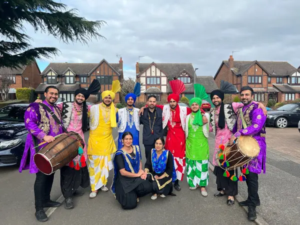 A bhangra group with dhols posing outside a family home