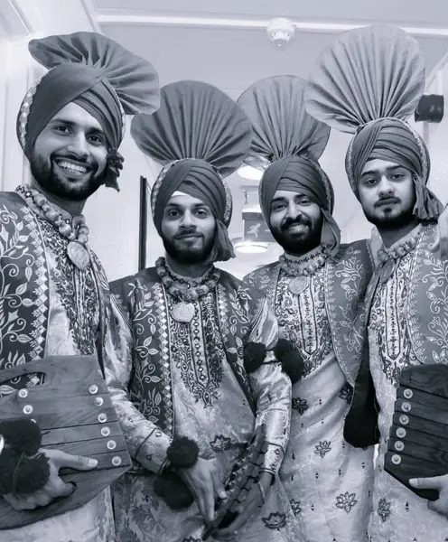 Black and white portrait of four bhangra dancers with chimtas and saaps