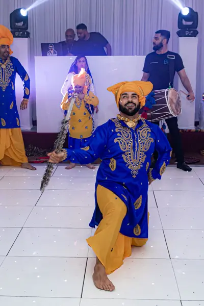 Bhangra dancer kneeling mid-routine on a white dance floor