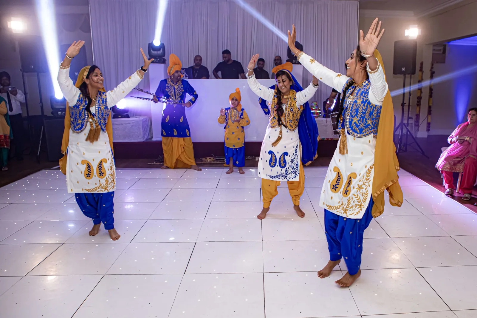 Male and female bhangra dancers performing on a white dance floor
