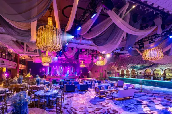 Ballroom with draped ceiling, gold chandeliers and purple and blue lighting