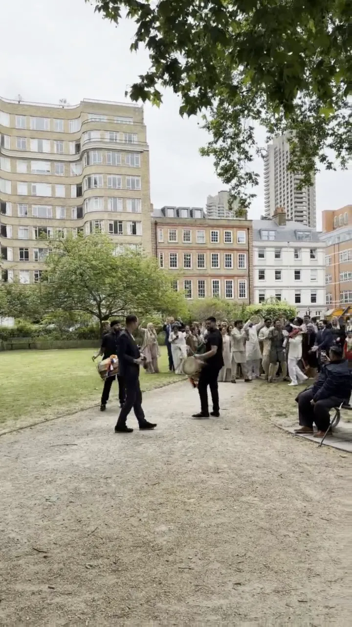 Two dhol players leading a baraat through a London garden square