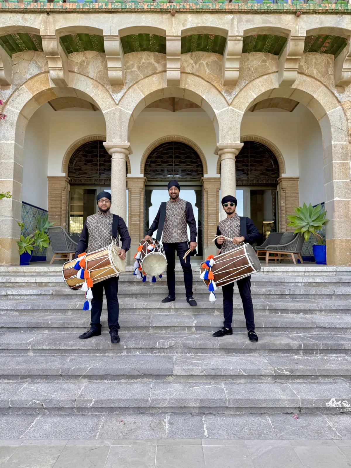 Three dhol players on the steps of a venue in Spain