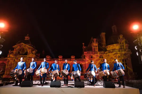 Dhol players performing on stage outside a floodlit chateau at night