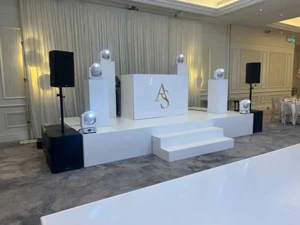 White DJ booth on a small stage with speakers and lights