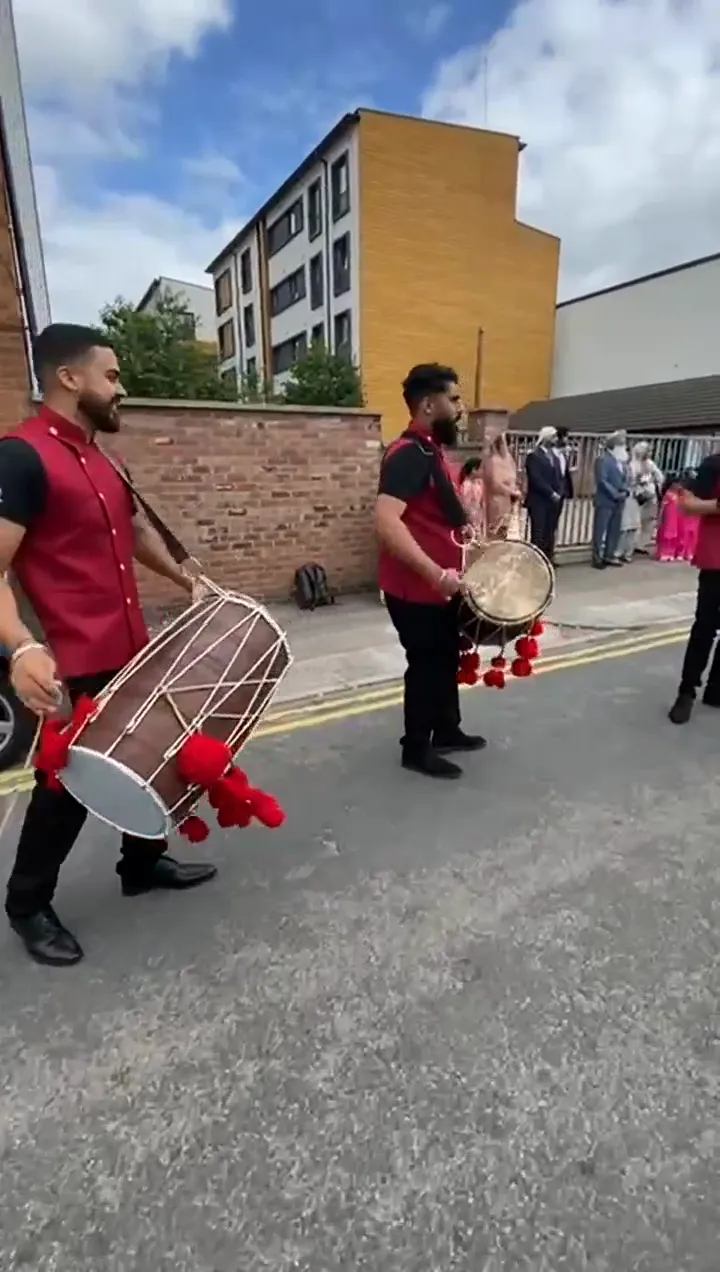 Band baja and dhol players in red sherwanis leading a baraat