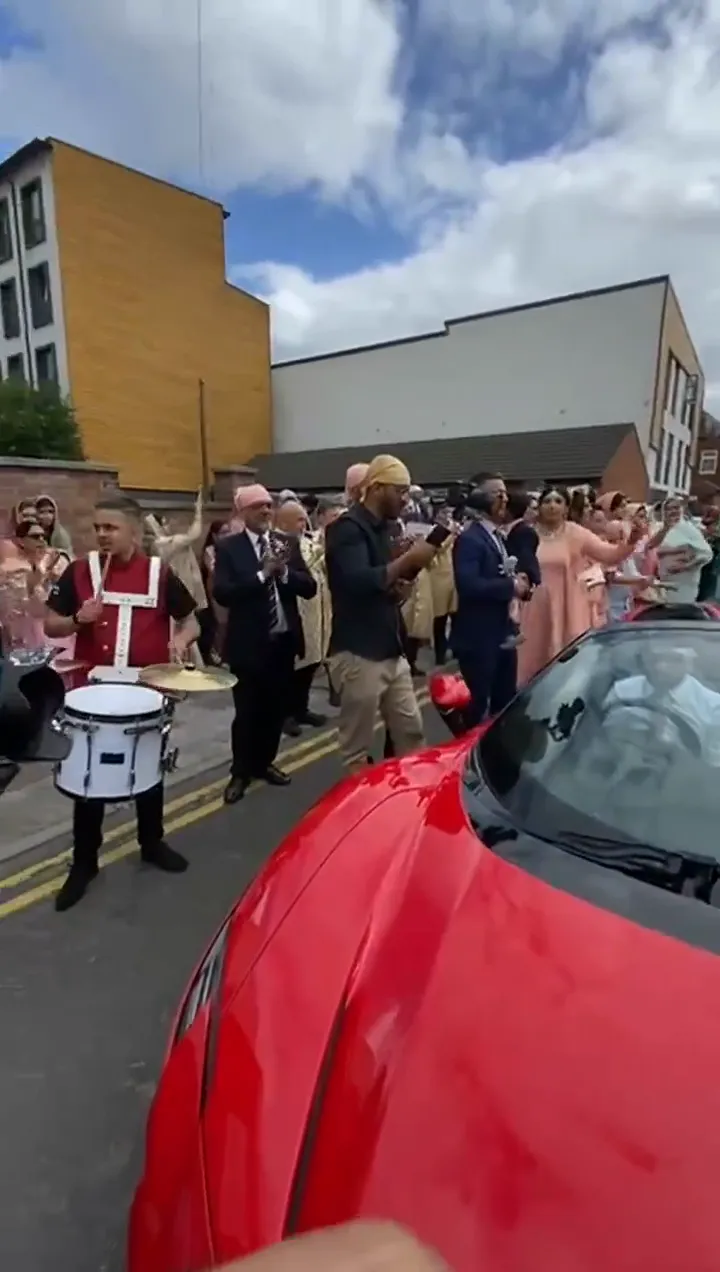 Band baja and dhol players in red sherwanis leading a baraat