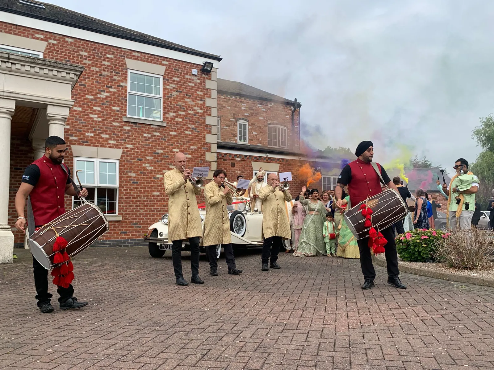 Band baja in red sherwanis leading the groom's party with coloured smoke