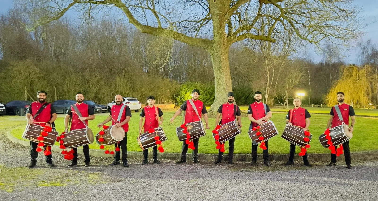 Band baja and dhol team in red sherwanis lined up on a lawn