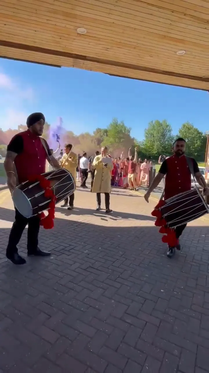 Band baja and dhol players in red sherwanis leading a baraat