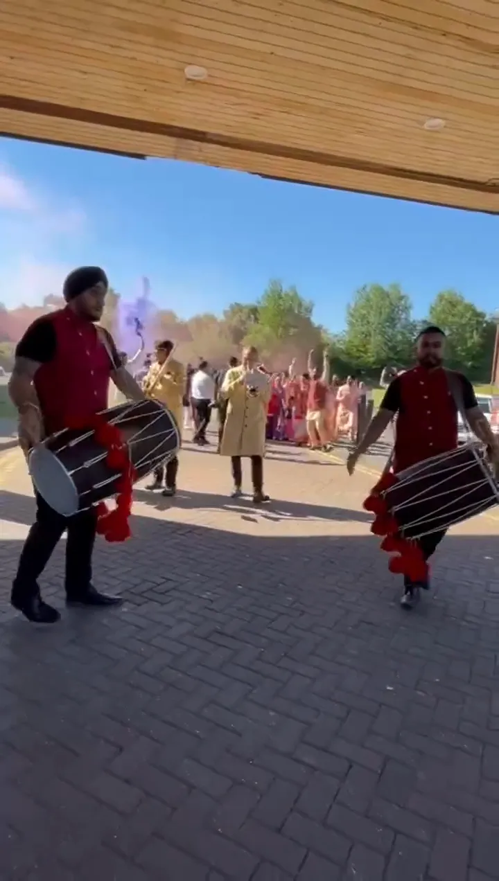 Band baja and dhol players in red sherwanis leading a baraat