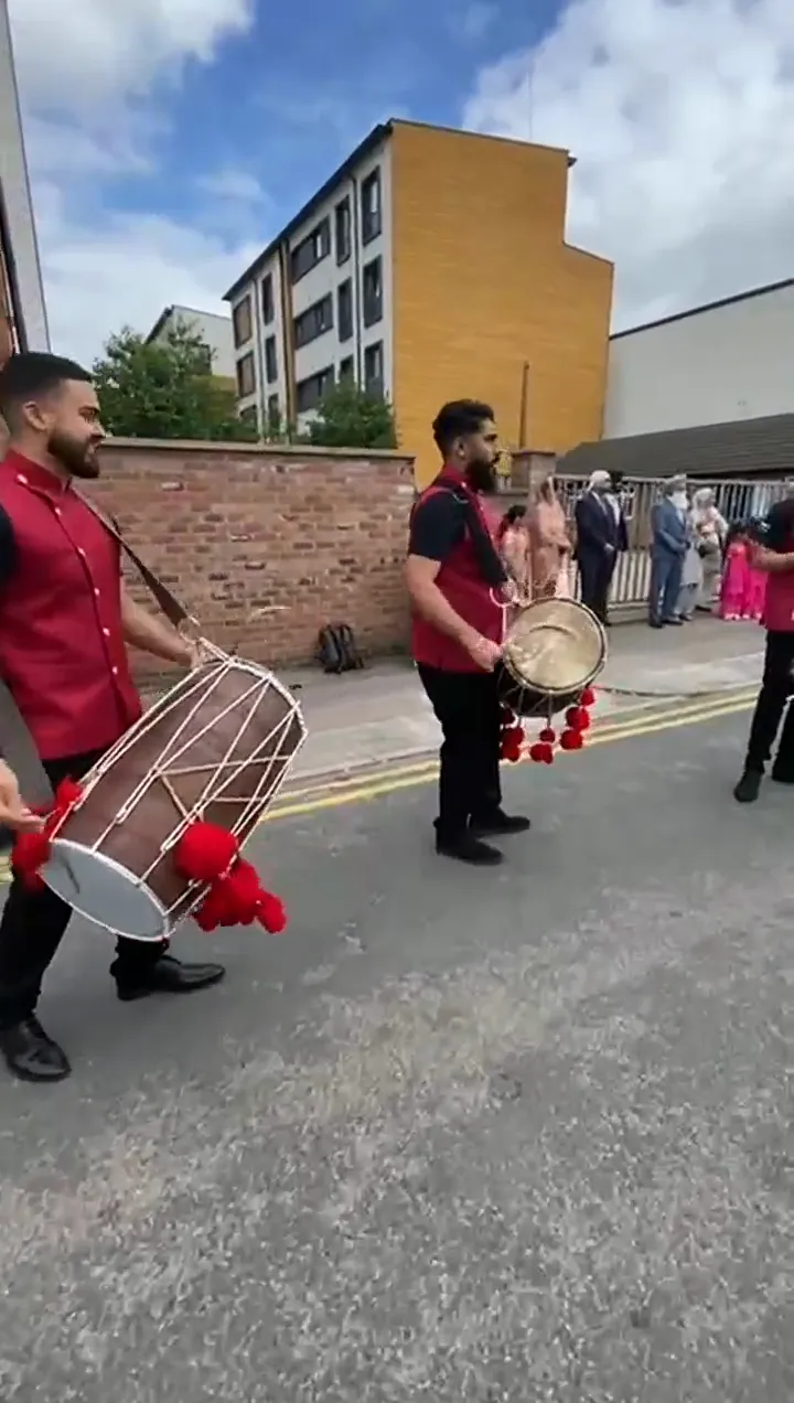 Band baja and dhol players in red sherwanis leading a baraat