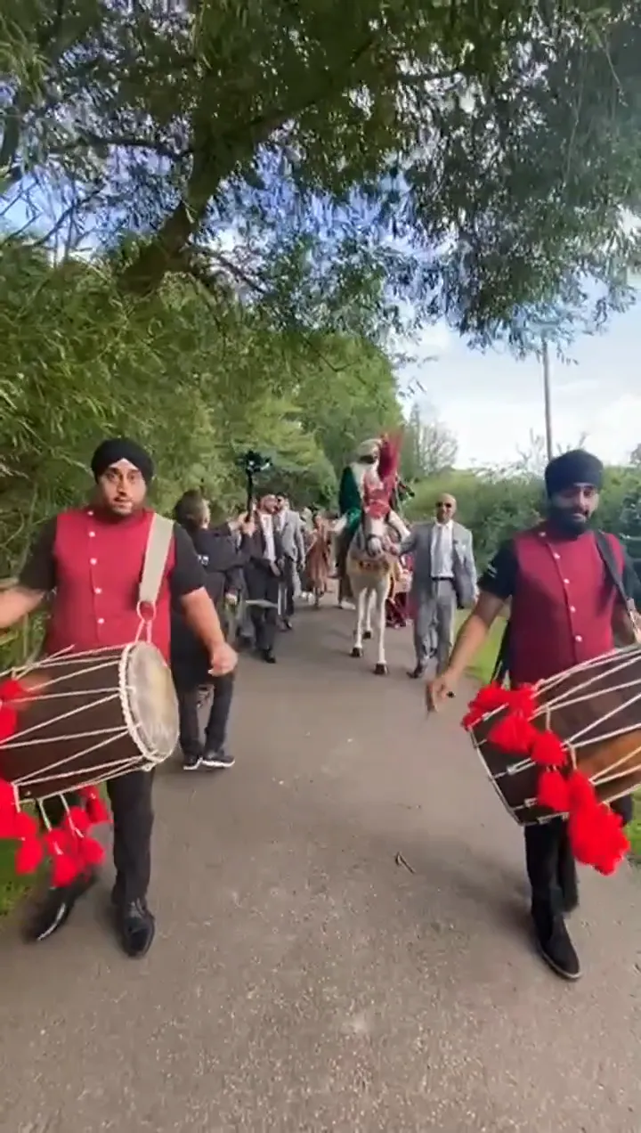 Band baja and dhol players in red sherwanis leading a baraat