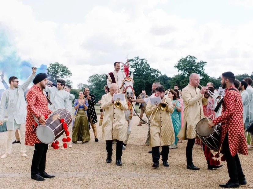 Band baja and dhol in red leading a baraat with the groom