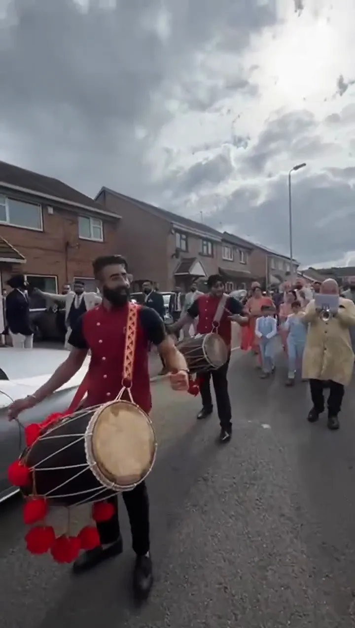 Band baja and dhol players in red sherwanis leading a baraat