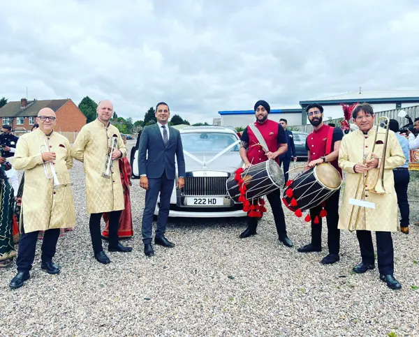 Band baja in red with the groom and family beside a wedding car