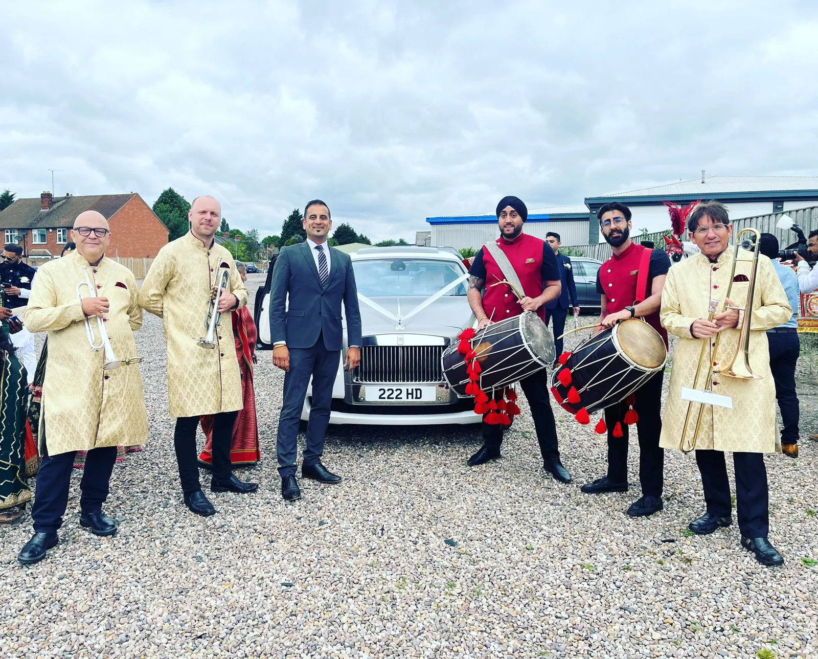 Band baja in red with the groom and family beside a wedding car