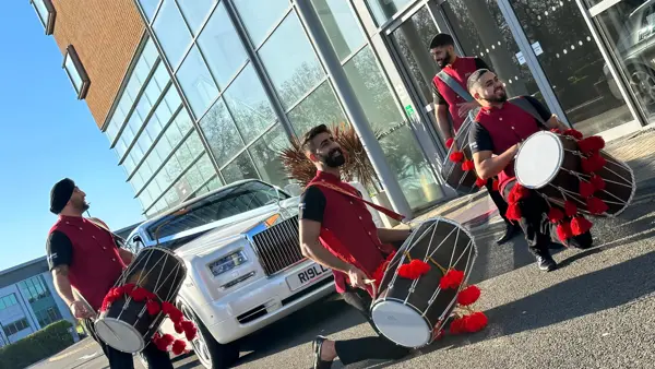 Dhol and band baja in red beside a white wedding car