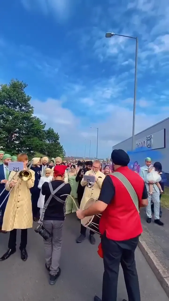 Band baja and dhol players in red sherwanis leading a baraat