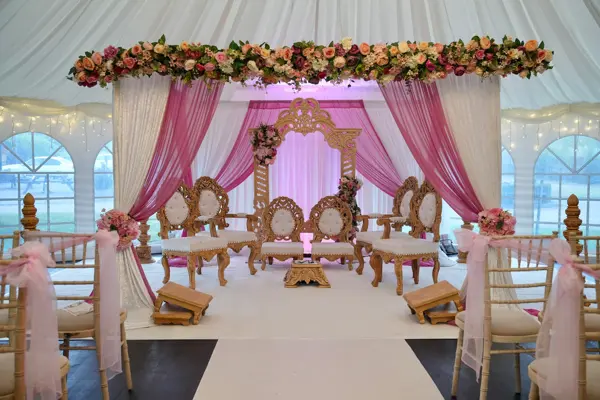 Mandap with pink drapes and floral canopy in a marquee