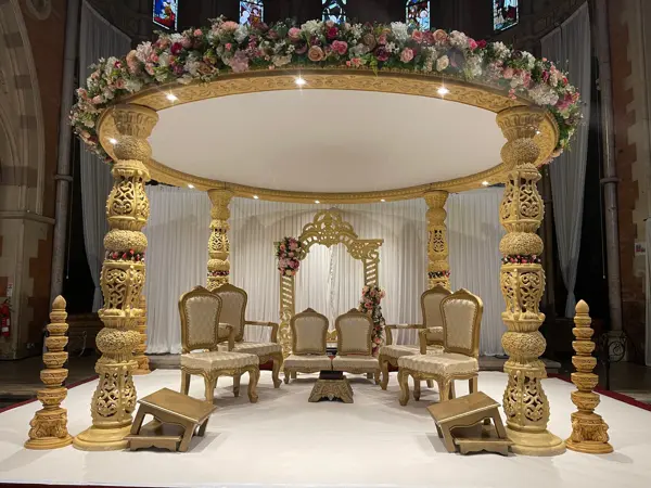 Round carved gold mandap with chairs and low stools
