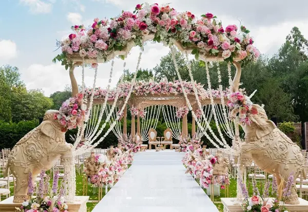 Outdoor floral mandap with carved elephants lining a white aisle