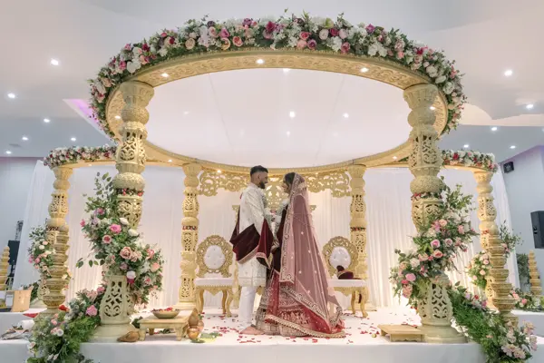 Bride and groom standing under a gold mandap