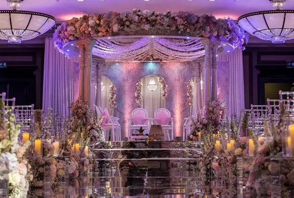 Mandap in a ballroom washed in purple light with floral arrangements