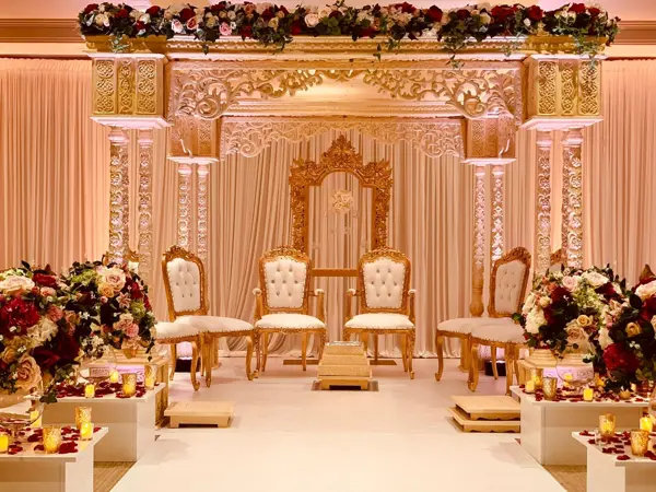 Gold carved mandap with ivory chairs and floral displays