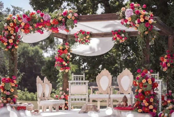 Outdoor mandap dressed in red and pink flowers with ivory chairs