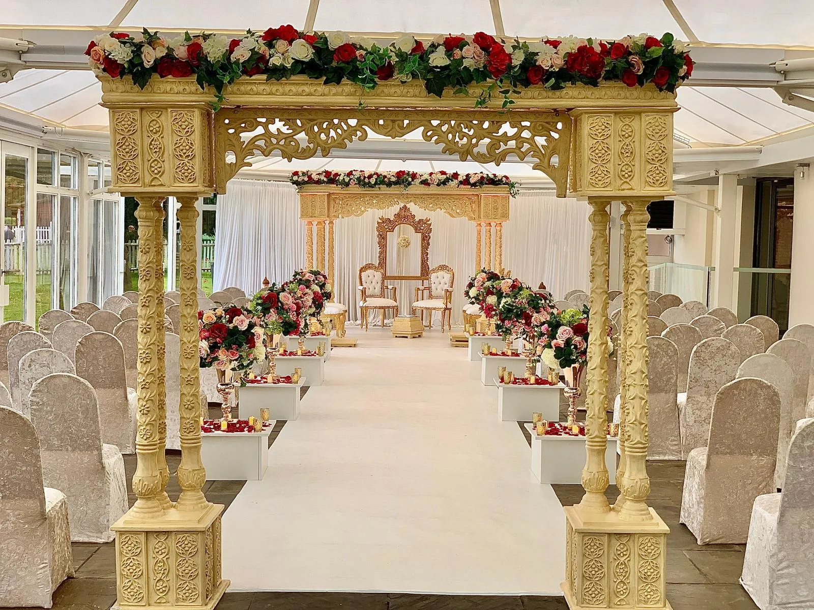 Carved gold pillared mandap with floral canopy and a long white aisle