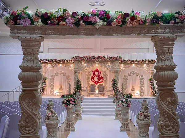 A stage mandap seen through tall carved pillars and floral urns