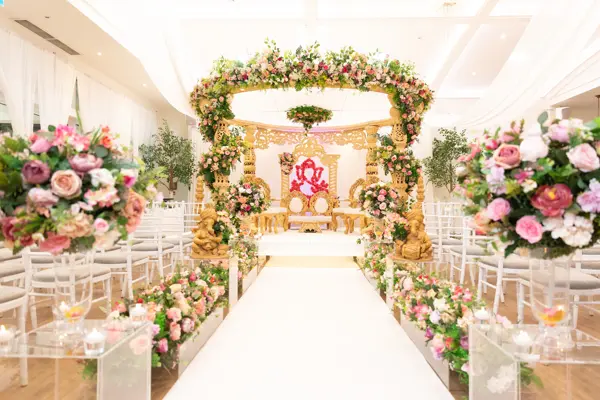 Gold mandap at the end of an aisle lined with pink roses
