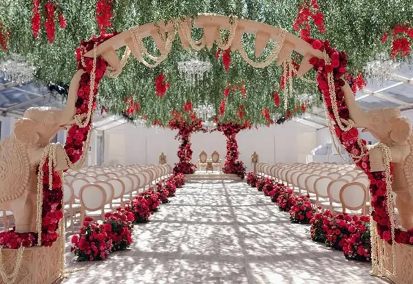 A walkway of red floral arches leading to the mandap