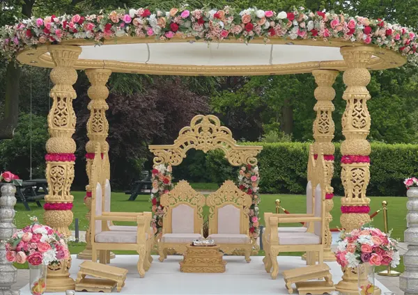 Carved gold mandap with pink roses set up in a garden