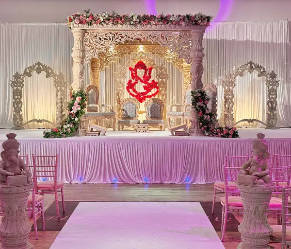 Carved mandap stage with a Ganesh backdrop and pink uplighting