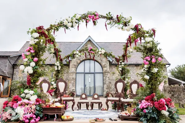 Mandap with a large floral arch in front of a country house
