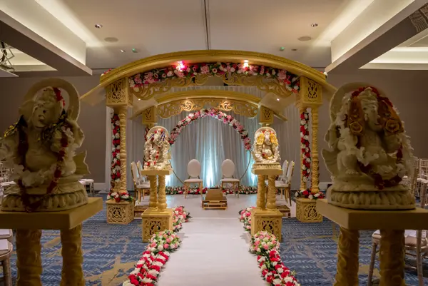 Gold mandap framed by large Ganesh statues and a rose petal aisle