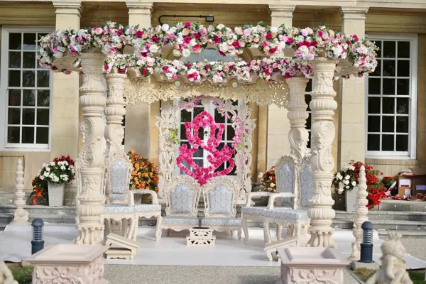 Carved mandap with floral canopy in a stone-pillared hall