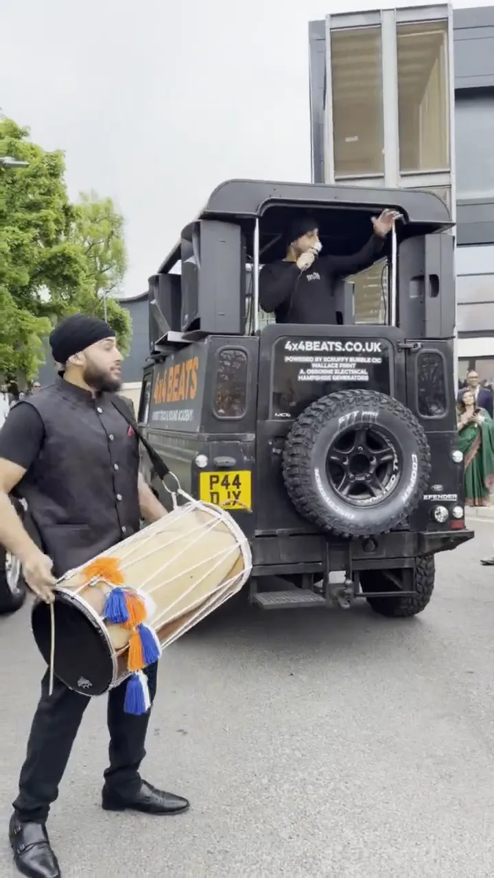 Dhol player and DJ truck leading a baraat through the streets