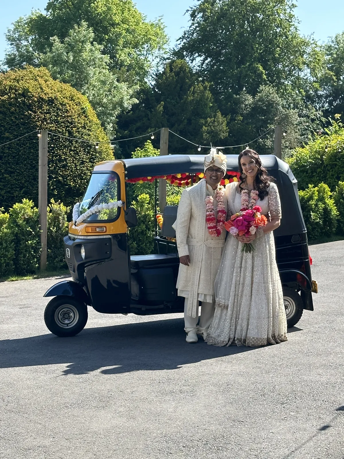 Bride and groom with a black and yellow tuk tuk in a garden