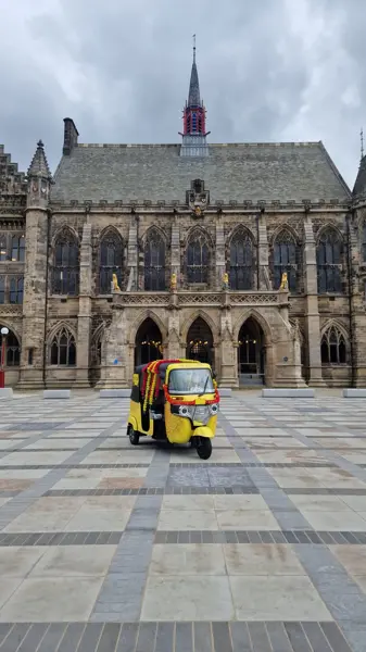 A decorated tuk tuk in front of a gothic town hall