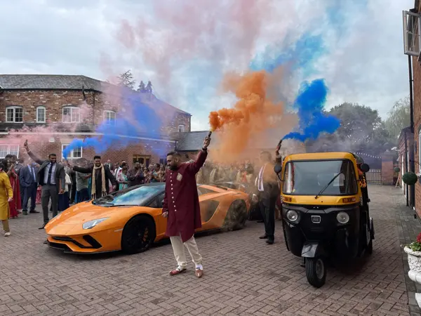 A tuk tuk arriving through coloured smoke with a groom and guests