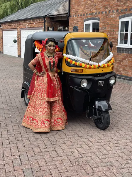 Bride in red lehenga next to a tuk tuk decorated with marigolds