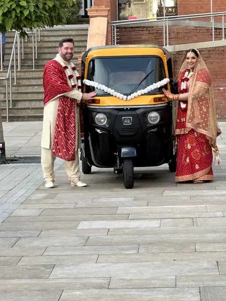 Bride and groom standing beside a tuk tuk with white flowers