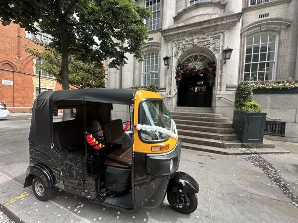 A garlanded tuk tuk parked outside a grand venue entrance