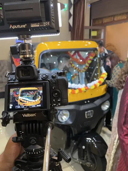 A garlanded tuk tuk seen through a videographer's camera screen