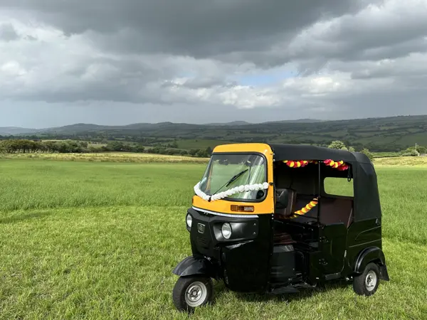 A tuk tuk with ribbons parked on open grass