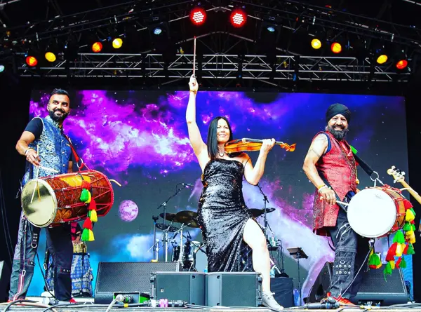 Violinist performing on a festival stage between two dhol players