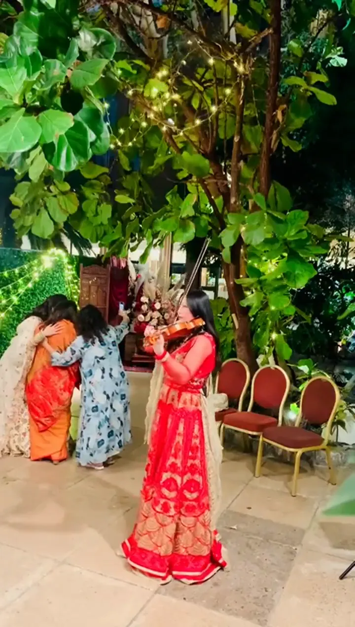 Violinist in a pink lehenga playing among guests